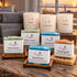Feierabend – Auszeit auf Vorrat von Friesenzart mit 2 × Naturseife Fährmann, 2 × Naturseife Seemann, 1 × Naturseife Deichgold, 1 × Duftkerze Ankerplatz, 1 × Duftkerze Kajüte, 1 × Duftkerze Treibholz, 2 × Gitter dunkel, 1 × Holzschale kompakt, 2 × Handtuch Grau. Beispielkombination; jede Kerzenglasfarbe unabhängig frei wählbar.