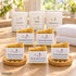 Sanfte Auszeit – Pflegevorrat von Friesenzart mit 5 × Naturseife Sommersonne, 1 × Duftkerze Weite, 1 × Duftkerze Auszeit, 1 × Duftkerze Blütentraum, 2 × Holzschale rund, 2 × Handtuch Weiß. Beispielkombination; jede Kerzenglasfarbe unabhängig frei wählbar.